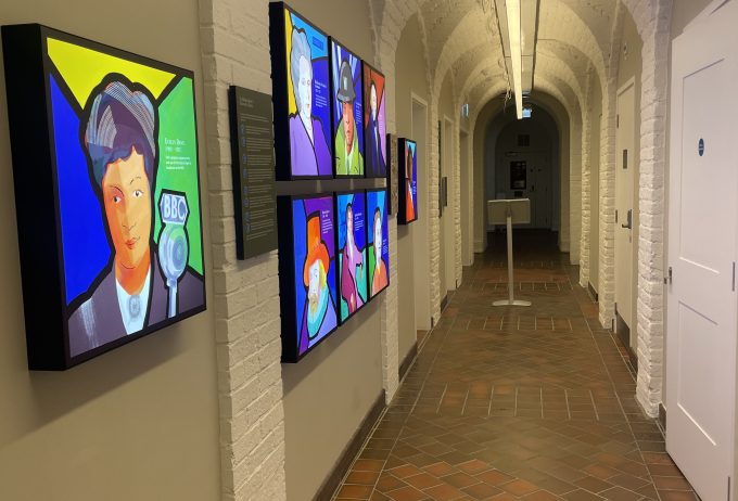 A corridor with bright tv screens on the left, displaying information.